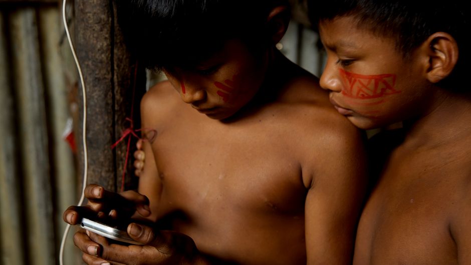 Yanomami Gold: Eine humanitäre Krise im Amazonas – Zwei indigene Kinder aus dem Amazonasgebiet erkunden drinnen ein Smartp…