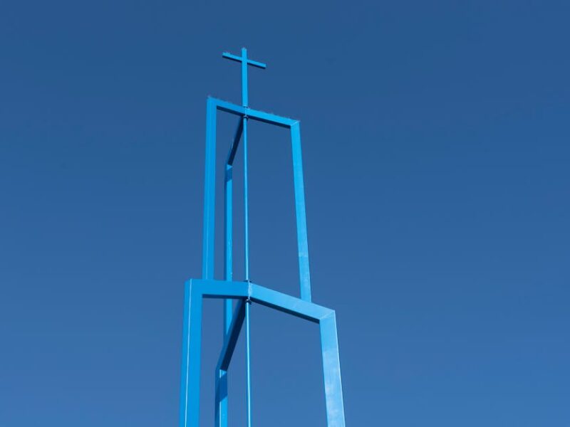 Der Great Circle von Newark: Heilige Geometrie – Ein minimalistischer blauer Kirchturm mit Kreuz vor klarem blauem Himmel …