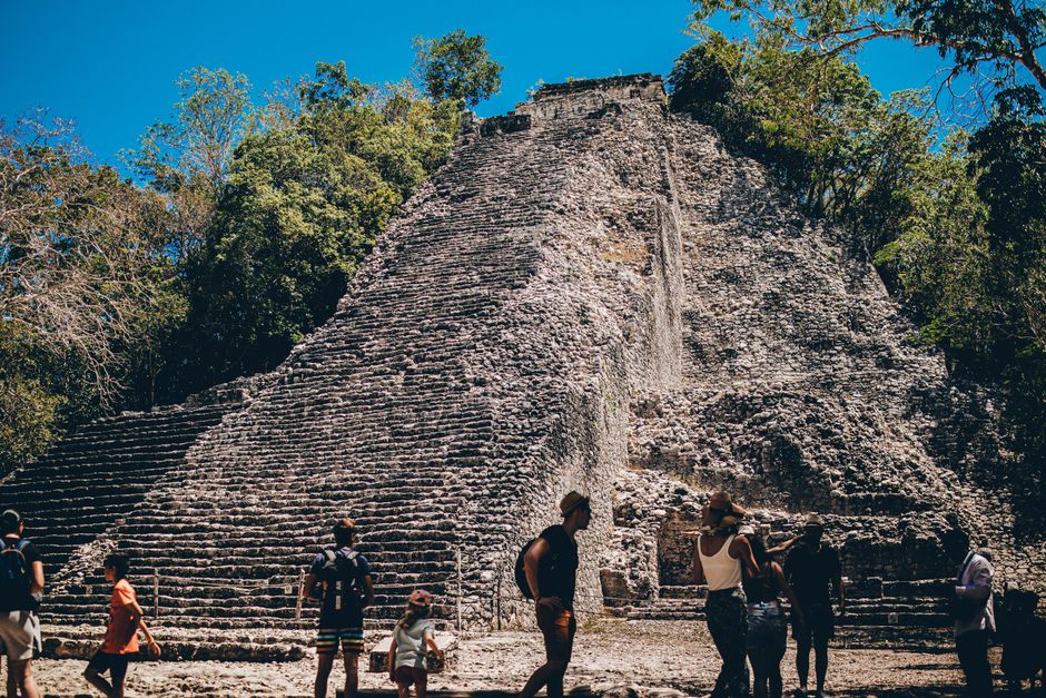 Cobá Reise: Ihr Guide zur Maya-Stätte in Quintana Roo – Besucher am Fuße einer alten Maya-Pyramide unter einem klaren blau…