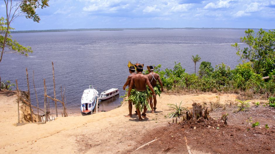 Manaus: Tor zum Amazonas – Ihr Guide zur Dschungelmetropole – Indigene Männer in traditioneller Tracht, die Boote am Amazo…